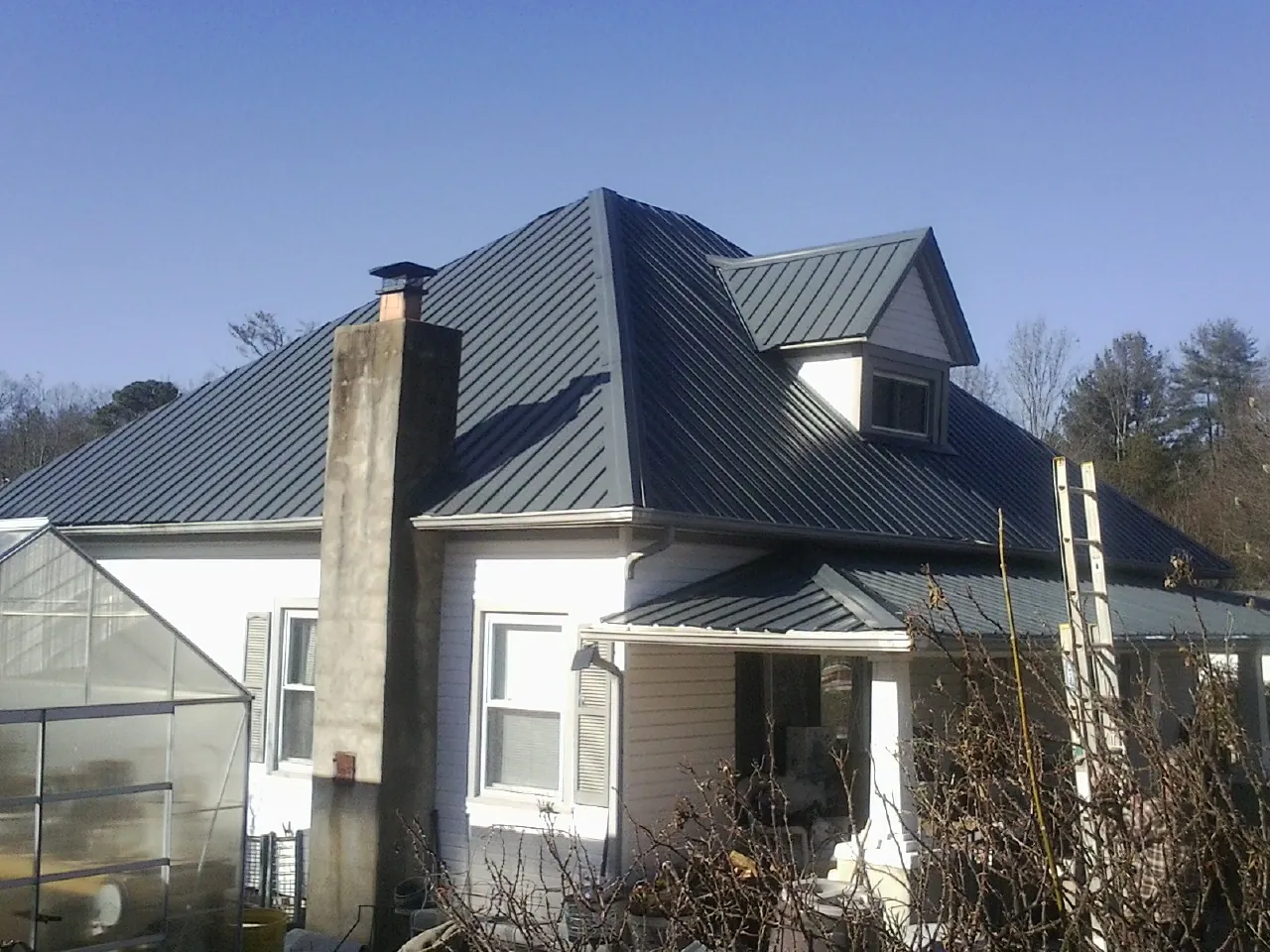 Dark blue standing seam metal roof on a white farmhouse with dormer — Slate & Tile Roof Repair by Roofing Brothers in Plum Branch