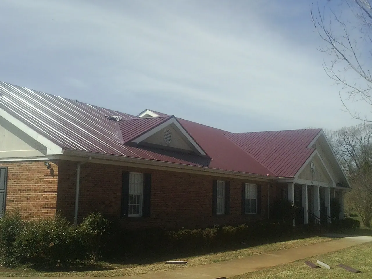 Red metal roof with gabled entries on a long brick building, from a Hail Damage Roof Repair job in Plum Branch