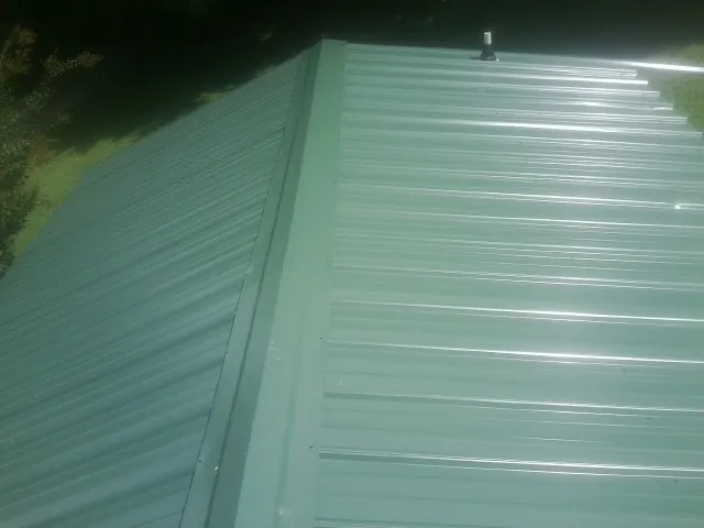 New green metal panels meeting at the ridge of a roof — Flat Roof Repair work by our crew in Plum Branch