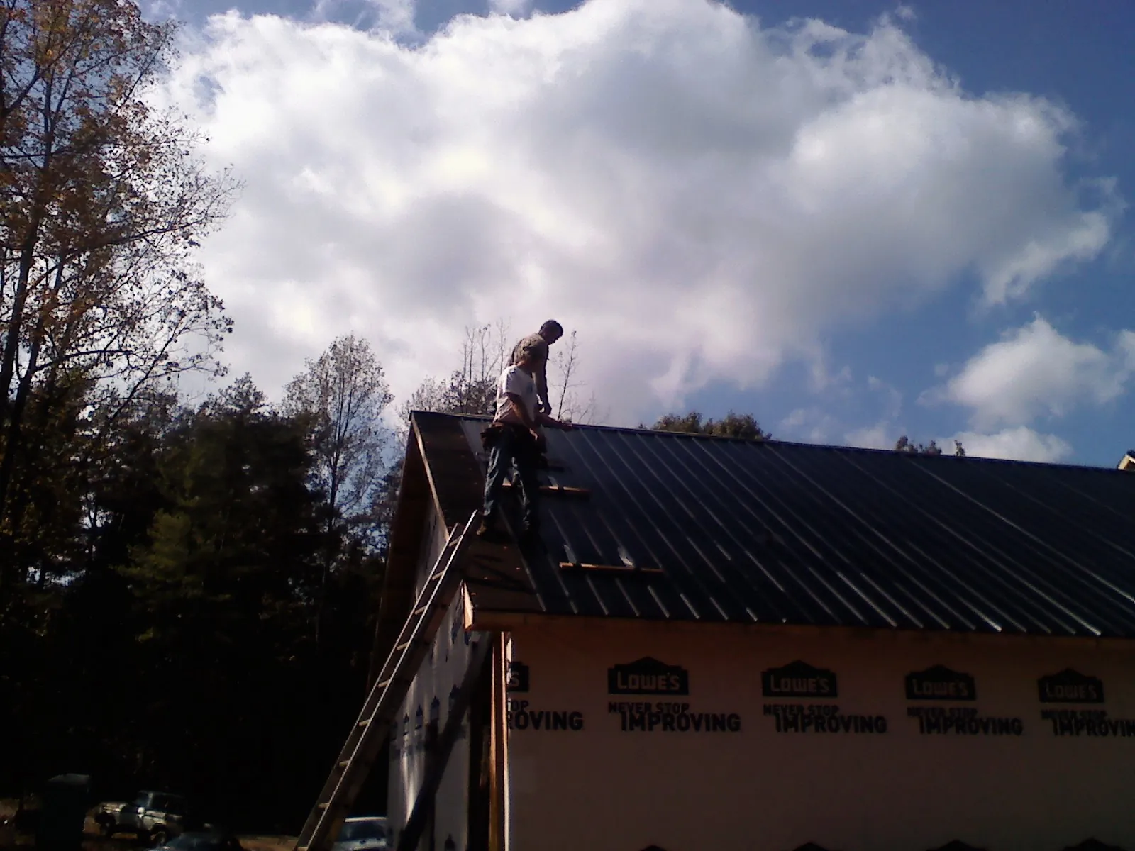 Roofer fastening dark metal panels high against a cloudy sky, from a Roof Inspection job in Plum Branch
