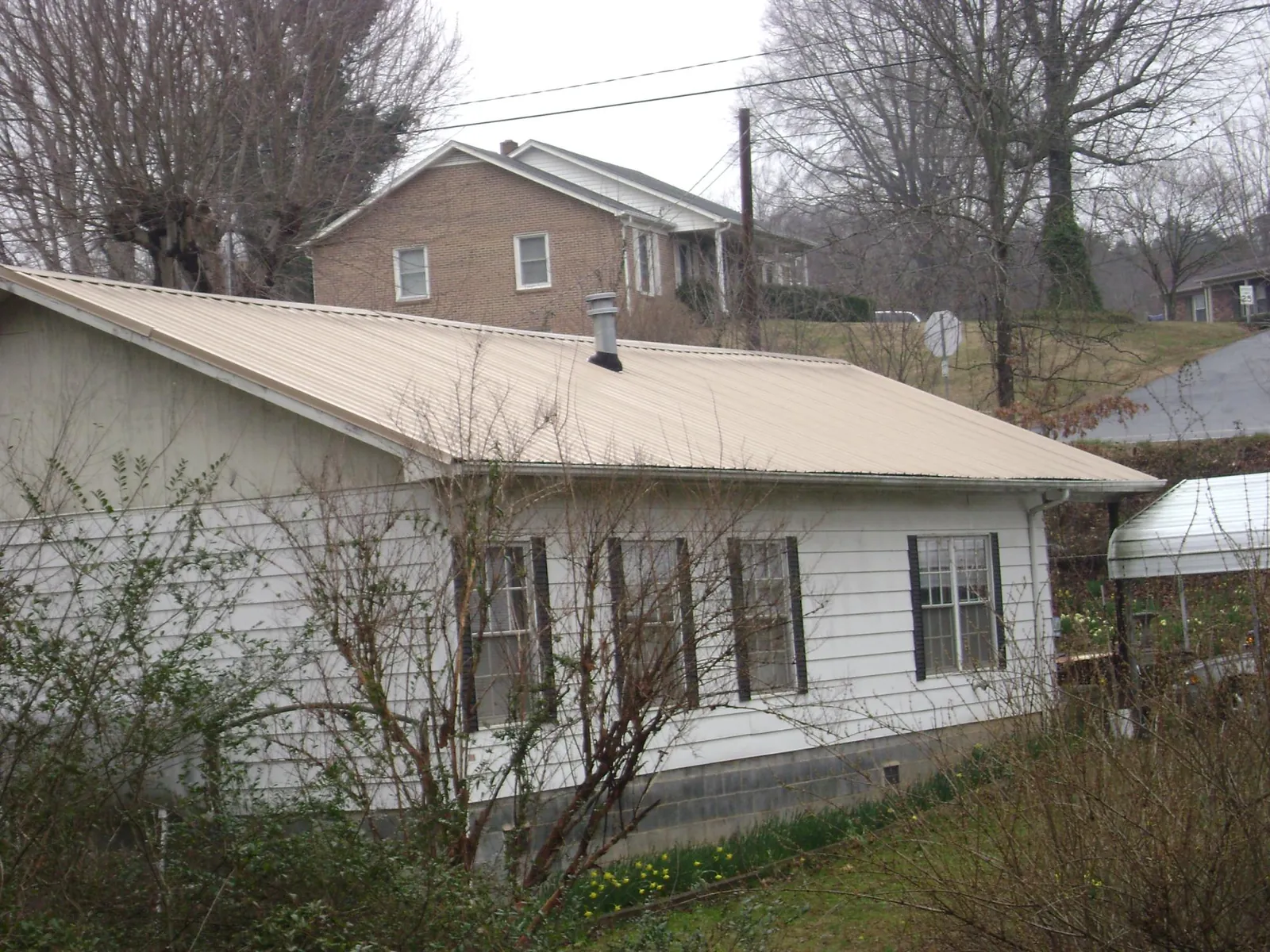 Tan metal roof on a white sided house set into a hillside — Commercial Roofing by Roofing Brothers in Plum Branch